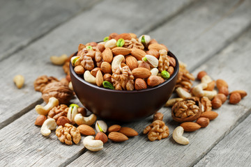 Wooden bowl with mixed nuts on a wooden gray background. Walnut, pistachios, almonds, hazelnuts and cashews, walnut.