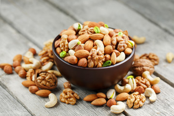 Wooden bowl with mixed nuts on a wooden gray background. Walnut, pistachios, almonds, hazelnuts and cashews, walnut.