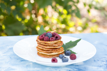 A stack of delicious pancakes with sour cream, raspberries and blueberries on a light background. with copy space