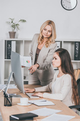 young businesswoman using desktop computer and mature female mentor pointing at screen