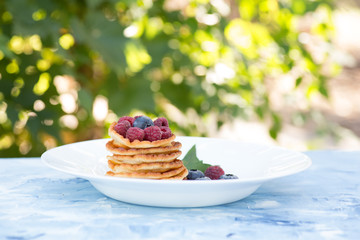 A stack of delicious pancakes with sour cream, raspberries and blueberries on a light background. with copy space