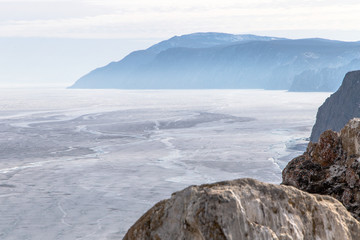 Cracks on the surface of the blue ice. Frozen lake in winter mountains. It is snowing. Lake Baikal. Winter