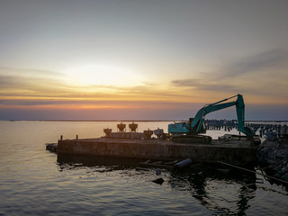 Obraz na płótnie Canvas Excavator Working construction bridge In the sea During the time of sunset.