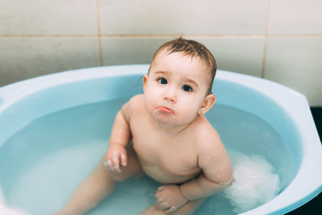 little girl baby is bathed in the blue basin in the bathroom is very fun