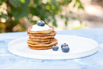 A stack of delicious pancakes with sour cream, raspberries and blueberries on a light background. with copy space