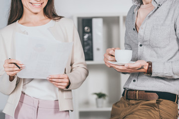 cropped shot of smiling business colleagues holding cup of coffee and papers in office