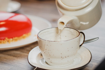 White ceramic teapot and cup on the table. Water is poured from the kettle. Against the background of reddish with icing.