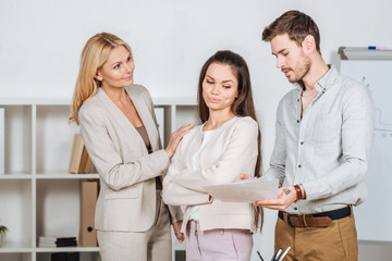 smiling female mentor looking at young colleagues with papers in office