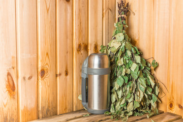 Thermos for tea with green birch broom in the bath