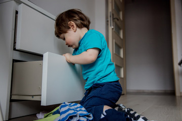 Little toddler boy play with clothes from cupboard at home