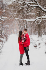 A date of lovers with my park in the winter. A bouquet of red flowers, walk, hug, kiss, laugh in a romantic setting. Portrait of a couple, husband and wife. Red jackets and coats.