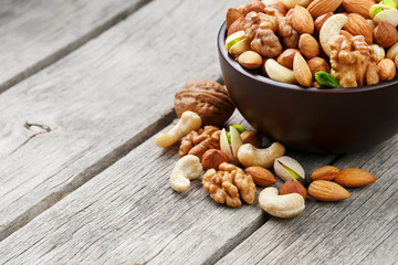 Wooden bowl with mixed nuts on a wooden gray background. Walnut, pistachios, almonds, hazelnuts and cashews, walnut.