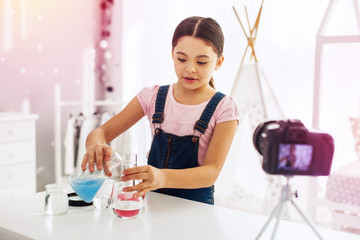 Schoolgirl filming video while making chemistry experiment with bright substances