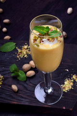 Mango yogurt dessert in a champagne glass topped with pistachios and mint against the dark background