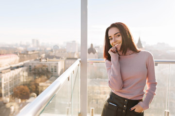 Stylish city portrait young fashionable brunette woman having fun on terrace on cityview background. Attractive businesswoman, cheerful mood, smiling to camera. Place for text