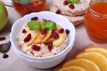 Porridge with caramelized apples and dried cranberries topped with mint surrounded by breakfast ingredients