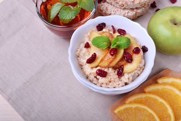 Porridge with caramelized apples and dried cranberries topped with mint surrounded by breakfast ingredients