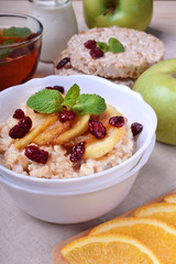 Porridge with caramelized apples and dried cranberries topped with mint surrounded by breakfast ingredients
