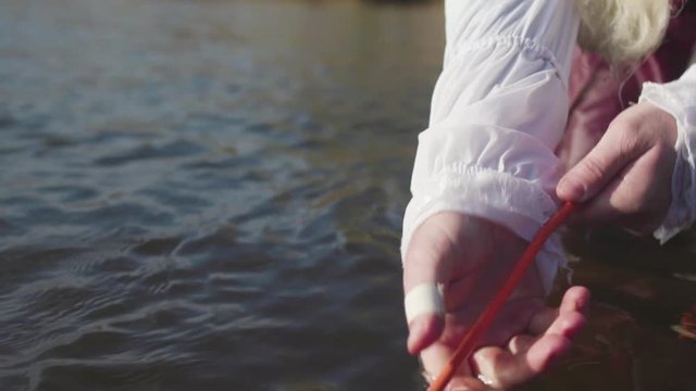 Ancient fishing technique, fisherman in old fashioned costume getting a fishing net. Stock. Man in old clothes of rococo manner pulling a fishing net, standing in the river in a sunny day.