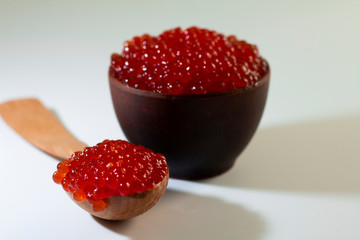 red caviar in a ceramic dish on a wooden platform on a white background