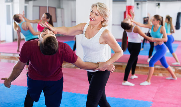 Sporty mature woman with her instructor are training self-defence moves in gym.