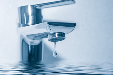 Faucet with water drop close up on blue background