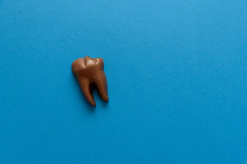 Bitten tooth from chocolate on blue paper background. Top view. Copy space. Healthy teeth, caries...