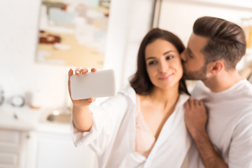 beautiful couple kissing and taking selfie on smartphone at home