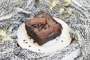 close up one piece of chocolate brownie with chocolate chip on white plate on fabric background, vintage style