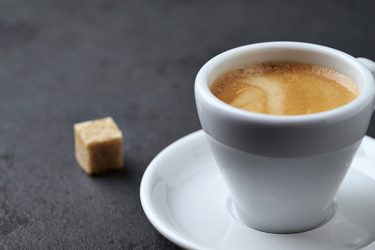 Cup of coffee and a brown sugar cube on black stone background. Close up. Copy space
