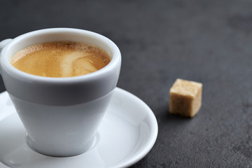 Cup of coffee and a brown sugar cube on black stone background. Close up. Copy space
