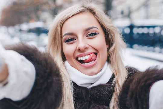 Beautiful girl takes funny winter selfie outdoor