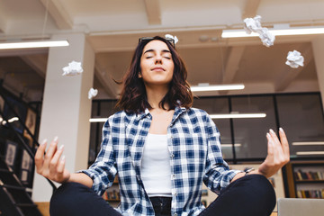 Relaxing time joyful young brunette woman having meditation on table in office surround flying...