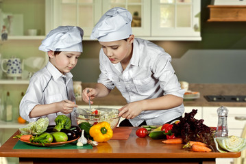 The boys in the cooks costumes cut the salad in the kitchen. Children prepare healthy food....