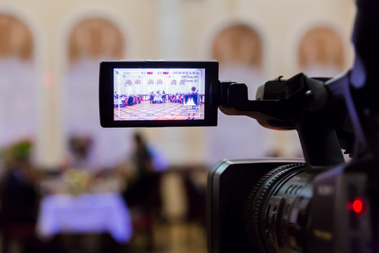 Video shooting at the event in the restaurant. Digital video camera with LCD display. People sit at tables in the background. Defocused background.