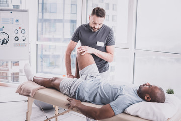 Attentive bearded man massaging leg of his client