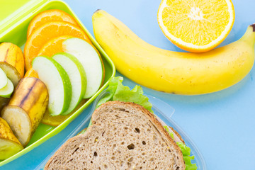 School lunch box. Bread, orange, candies, baby corns, carrot and tomatoes in green plastic container