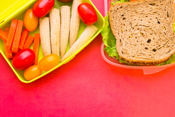 School lunch box. Bread, orange, baby corns, carrot and tomatoes in green plastic container