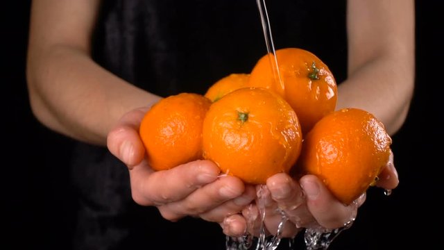 Washing orange tangerines in woman hands, slow motion