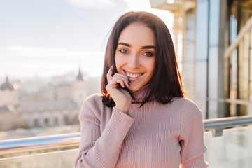 Fototapeta premium Portrait joyful smiled brunette young woman in sunny morning chilling on terrace. Smiling to camera, expressing positive face emotions, success, enjoying