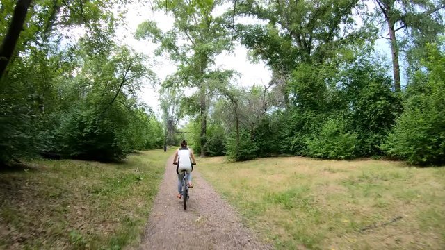 Cycling in the park. Girl riding a bike on a forest trail very quickly. Time lapse. Back view