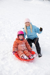 Fototapeta na wymiar Mom and daughter ride on a sled from a snow slide. Ride from a snow hill on a sled. Sleigh rides, winter fun, snow, family sleigh rides.