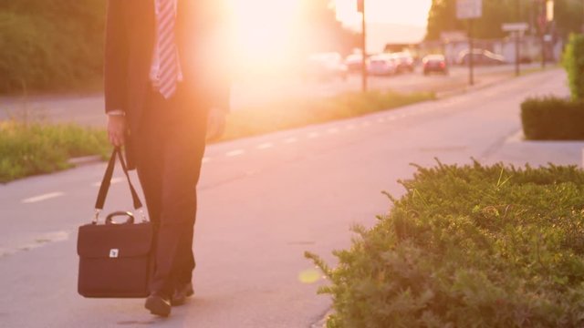 SLOW MOTION, LENS FLARE, LOW ANGLE: Sad young businessman carrying his briefcase after a bad day at work. Unrecognizable young man in a suit losing hope after another failed job interview in the city.