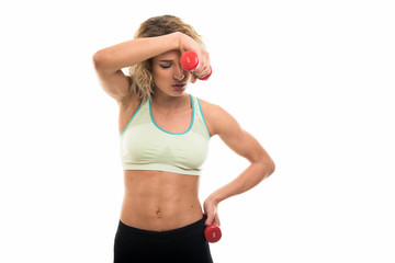 Beautiful young fit girl looking tired holding dumbbells