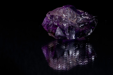 Rough cut big purple transparent stone with a black background reflecting in the surface it rests on
