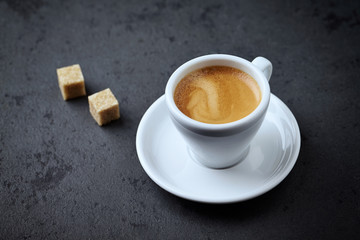 Cup of coffee and two brown sugar cubes on black stone background. Copy space.