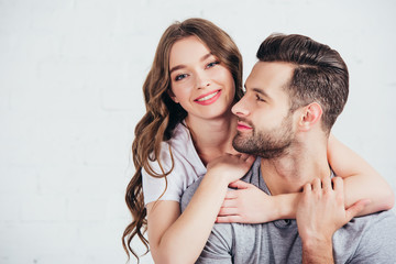 young loving couple gentle embracing and smiling near white wall with copy space