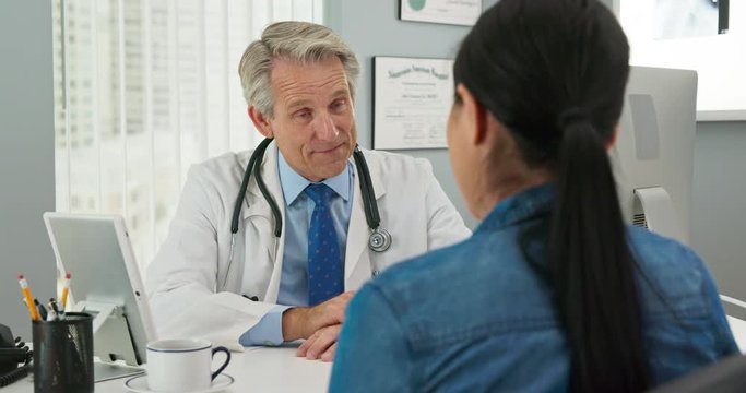 Mature Caucasian male doctor in his office listening to new patient and smiling