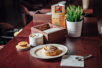 Round cinnamon bun in a plate on a dark wooden table in a cafe
