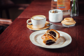 Puff pastry bun with liquid chocolate inside, lies in a plate on a dark wooden table in a cafe